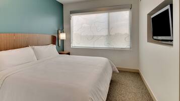 A hotel room with a large bed, a window with a view, a flat-screen TV mounted on the wall, and a nightstand with a lamp.