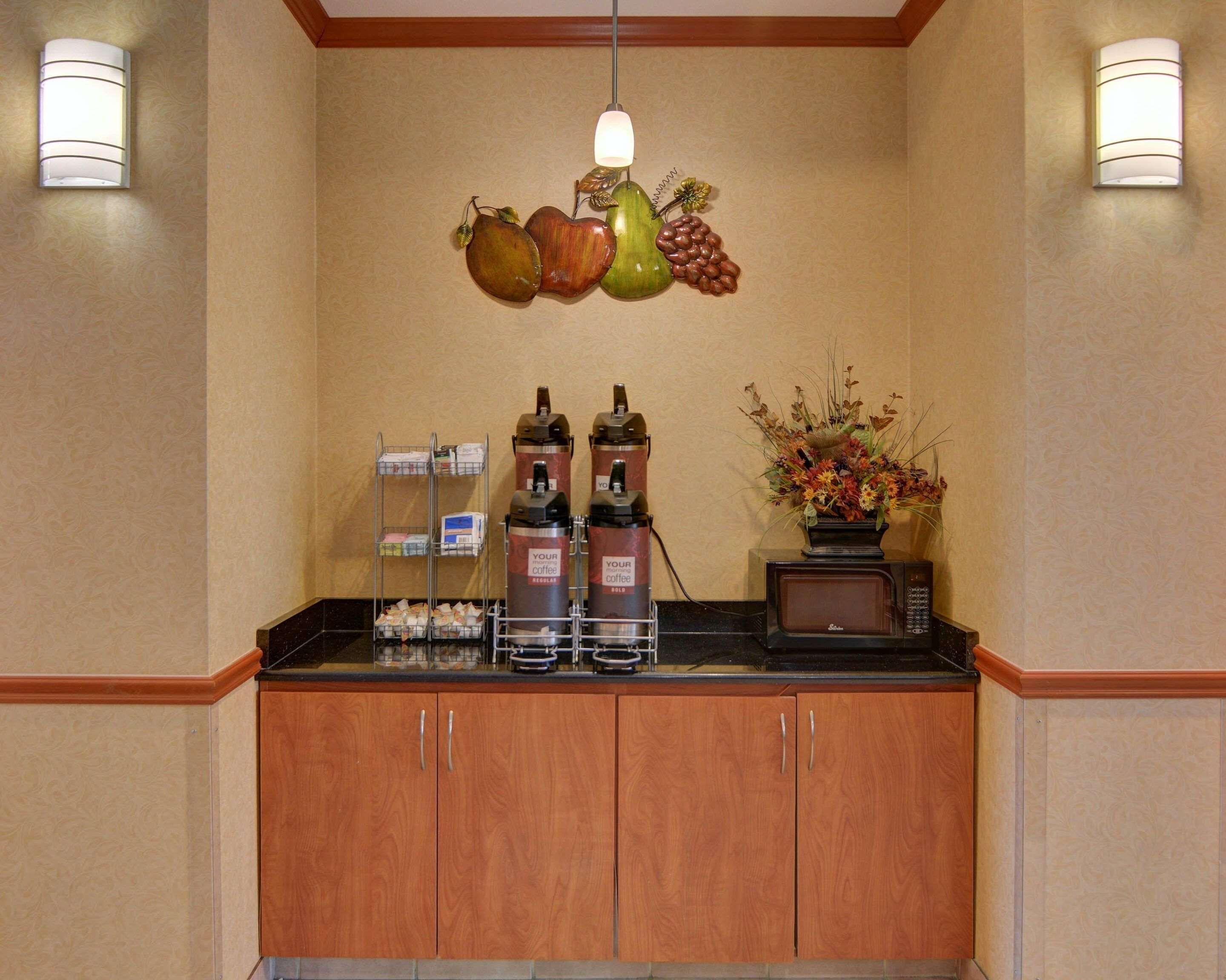 A coffee station with dispensers, a microwave, and a vase of flowers.