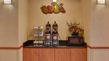A coffee station with dispensers, a microwave, and a vase of flowers.