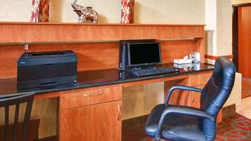Un bureau d’hôtel avec un bureau en bois, un ordinateur, une imprimante et un fauteuil de bureau noir.
