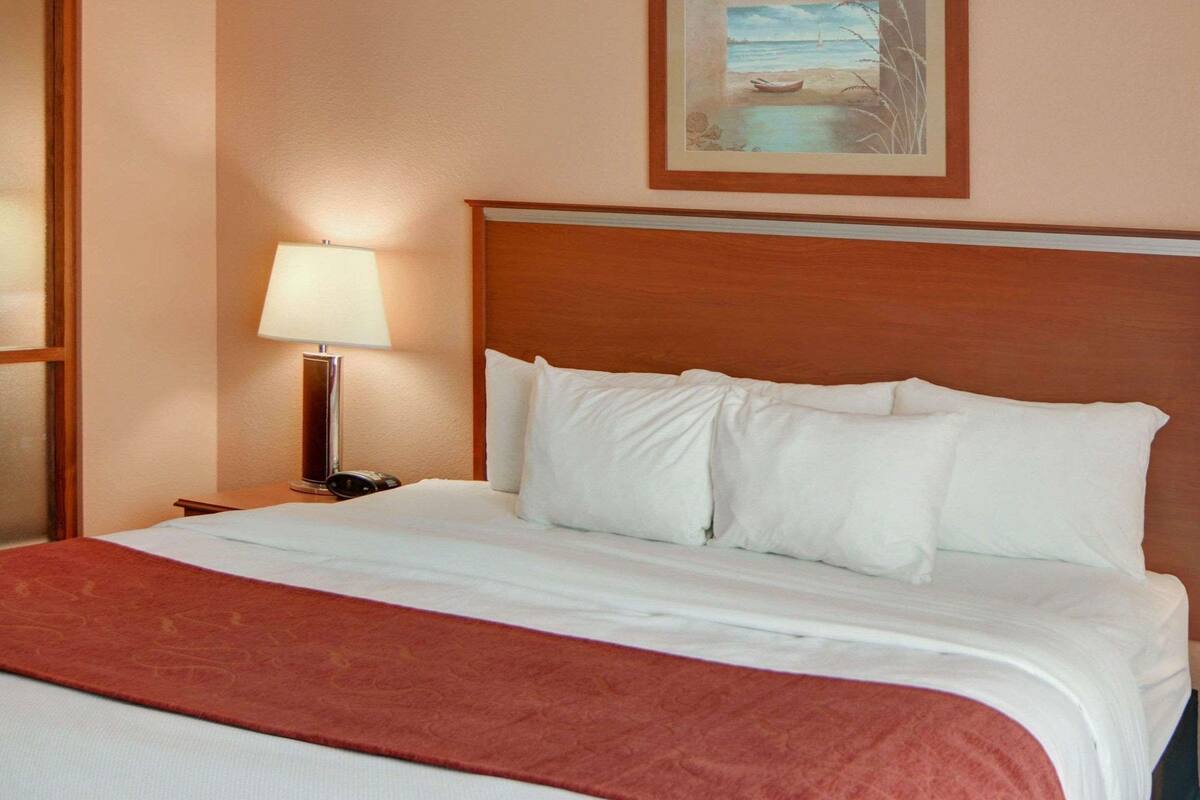 Hotellihuone, jossa on suuri sänky, yöpöytä lampun kanssa ja taulu seinällä.