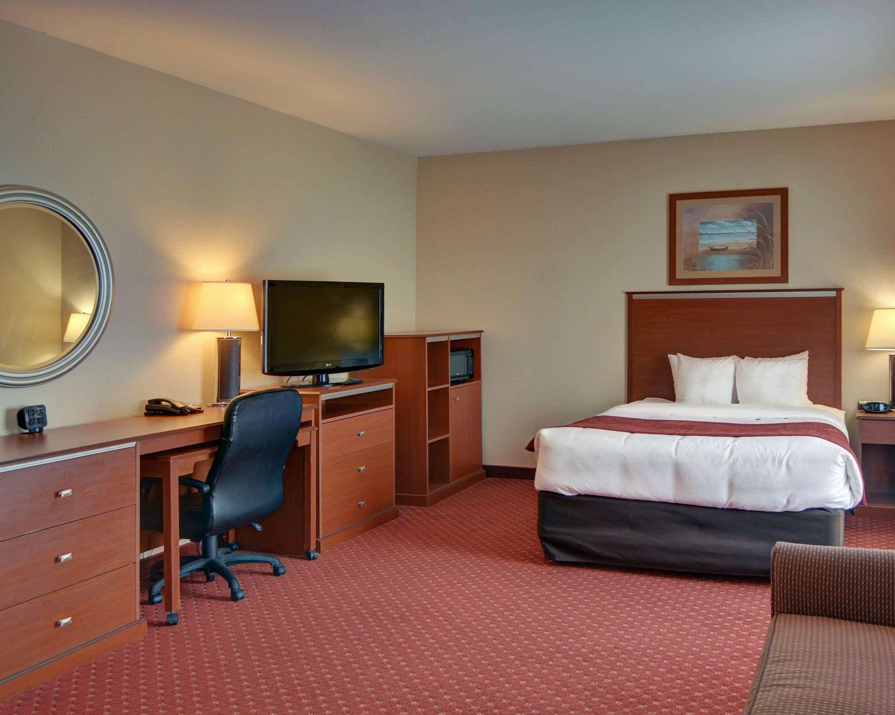 Una habitación de hotel con cama, escritorio, computadora, televisor, silla y lámpara.