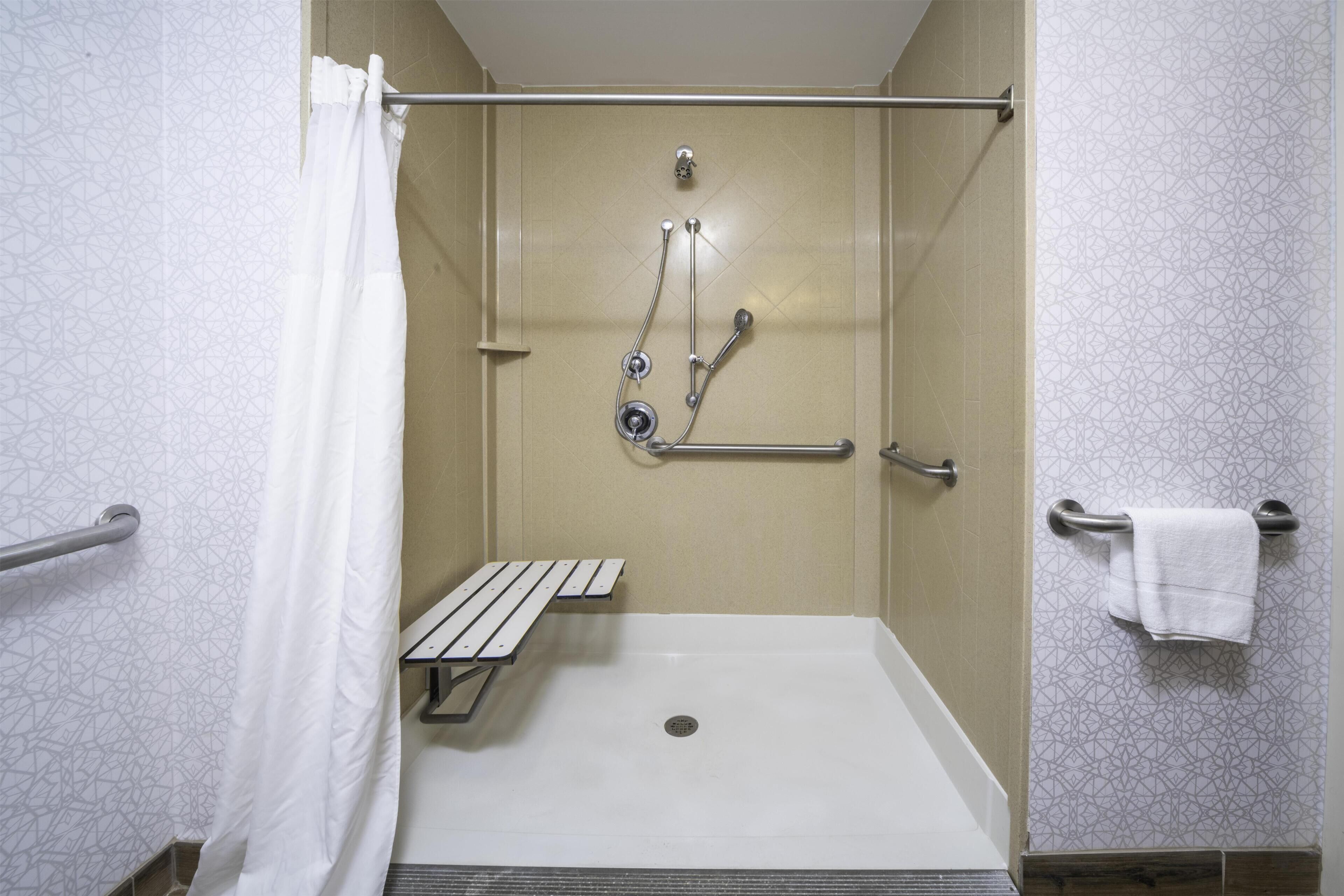 Een douche met een bankje, handgrepen en een handdoekhouder.