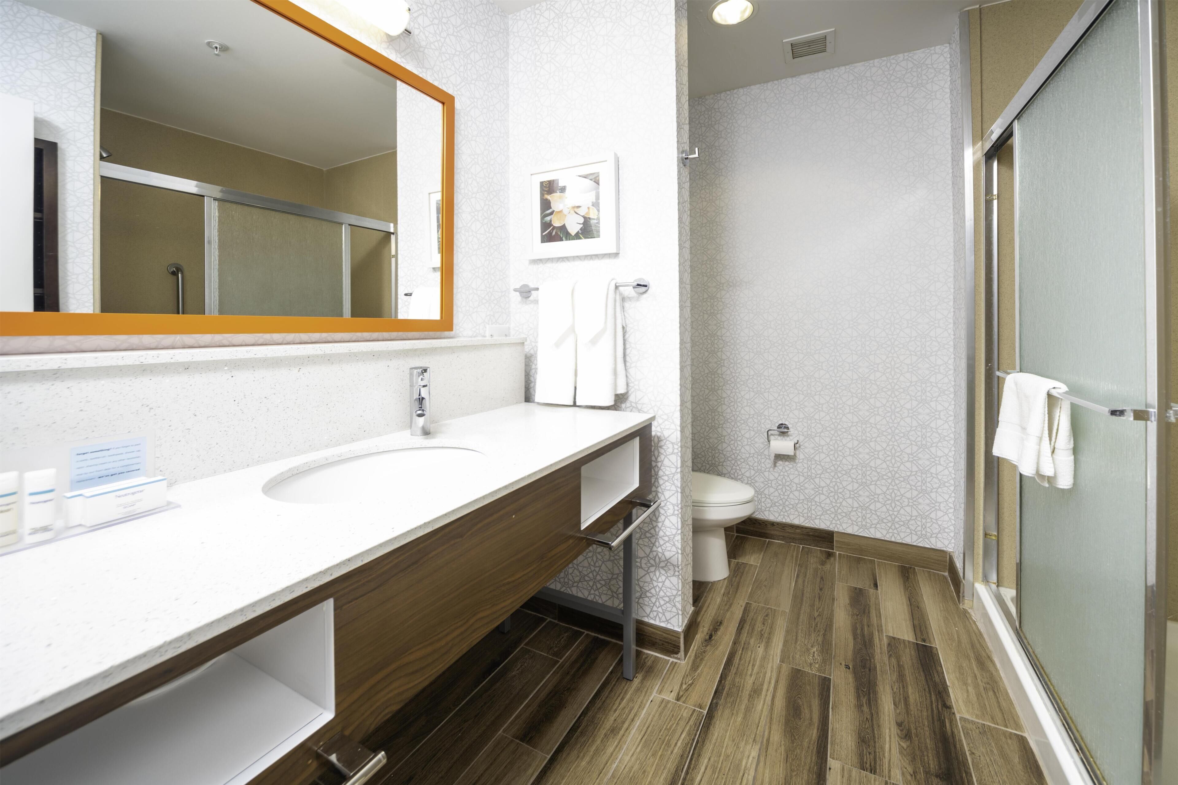 Un baño moderno con tocador de madera, un espejo grande, inodoro y cabina de ducha con mampara de vidrio.