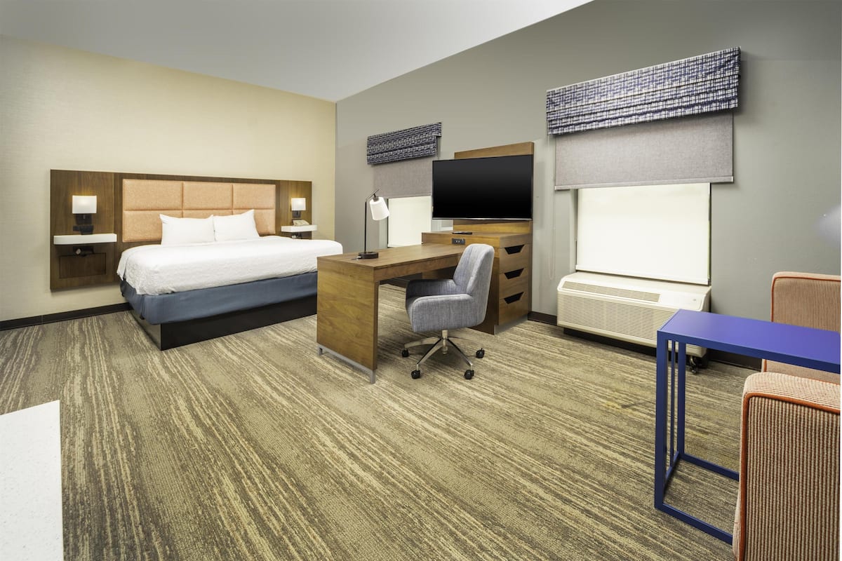 Una habitación de hotel con cama, escritorio, silla, televisión y aire acondicionado.