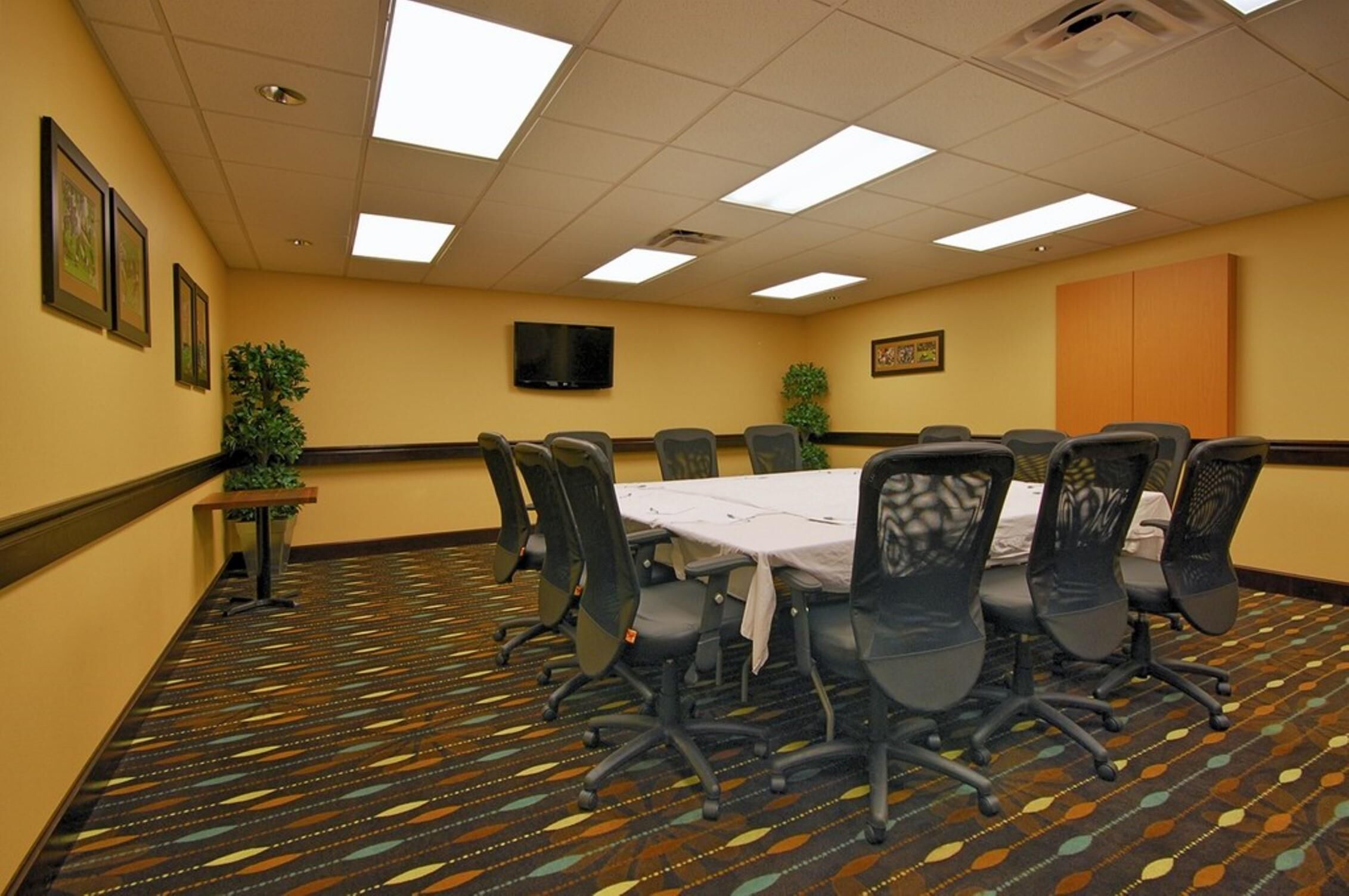 Una sala conferenze con un lungo tavolo, sedie, una TV, quadri incorniciati e un tappeto decorato.