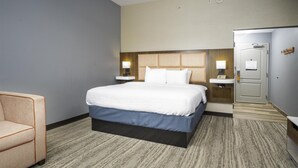Ein Hotelzimmer mit Bett, Stuhl, Nachttisch, Lampe und einer Tür.