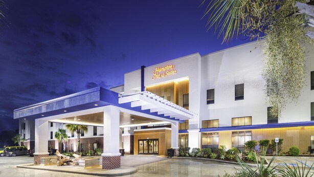 Ein modernes Hotel mit einer markanten Eingangspartei, einem überdachten Außenbereich und einem Schild mit der Aufschrift 'Hampton Inn & Suites'.