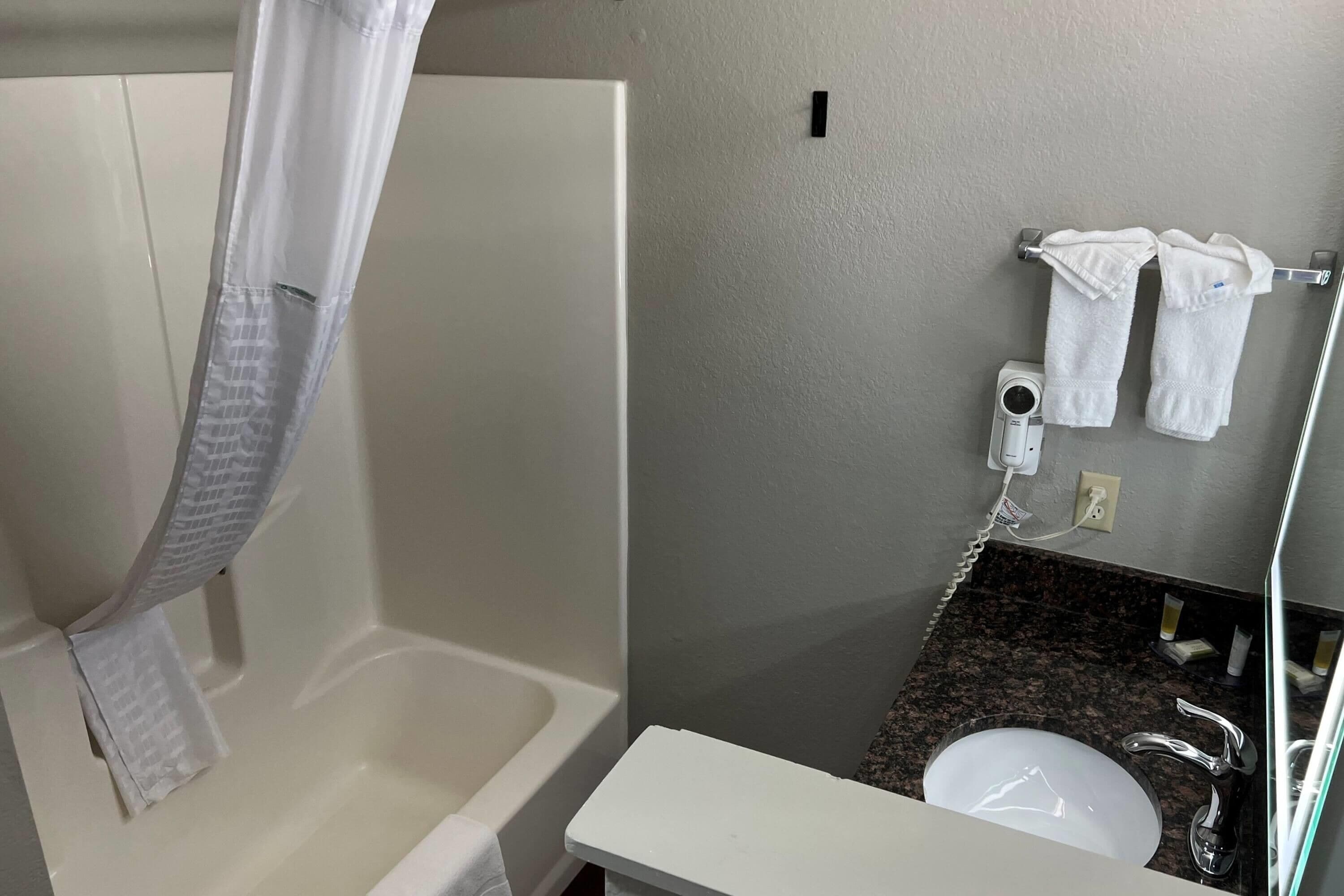 Un baño con bañera, cortina de ducha, toallero con dos toallas, lavabo y espejo.