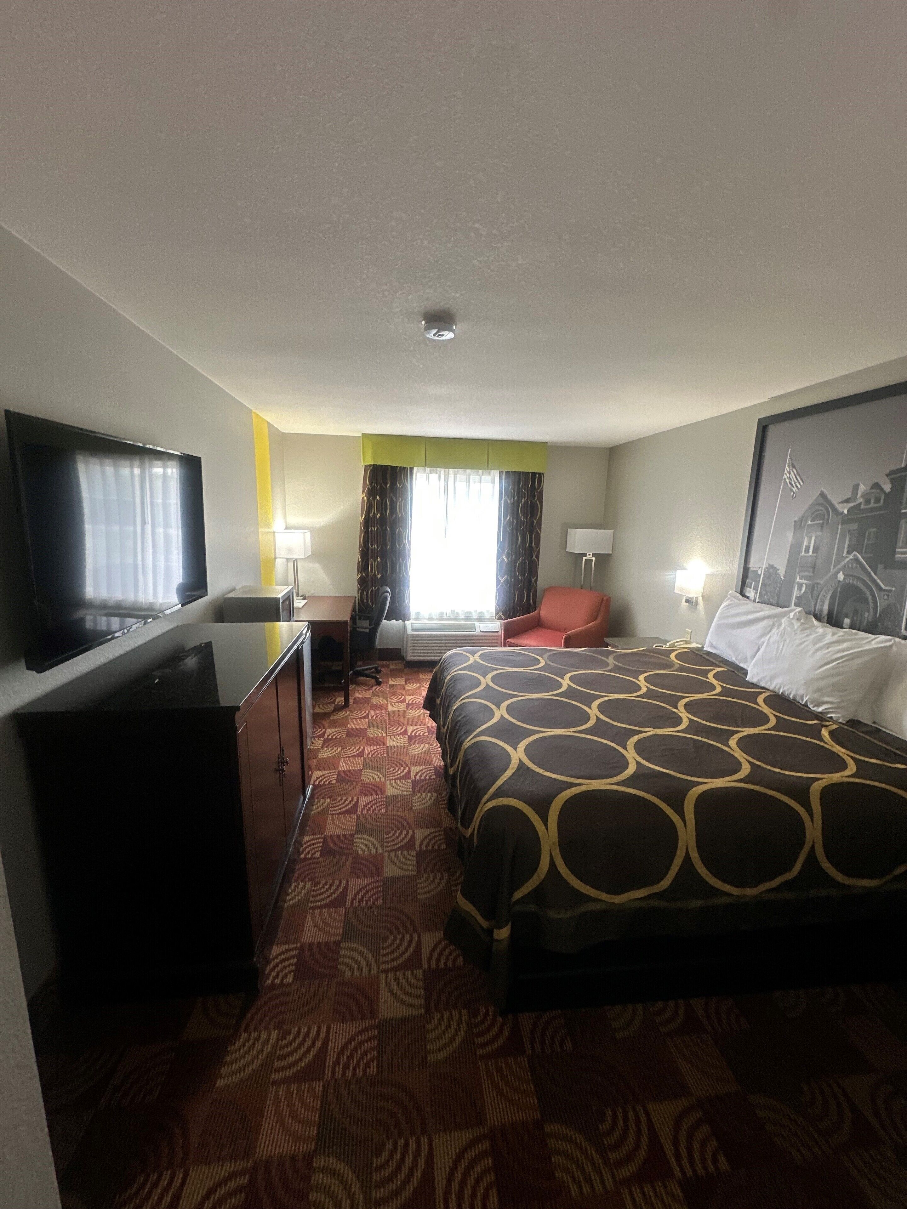 Habitación de hotel con una cama grande, un escritorio con silla, un televisor y una ventana con cortinas.