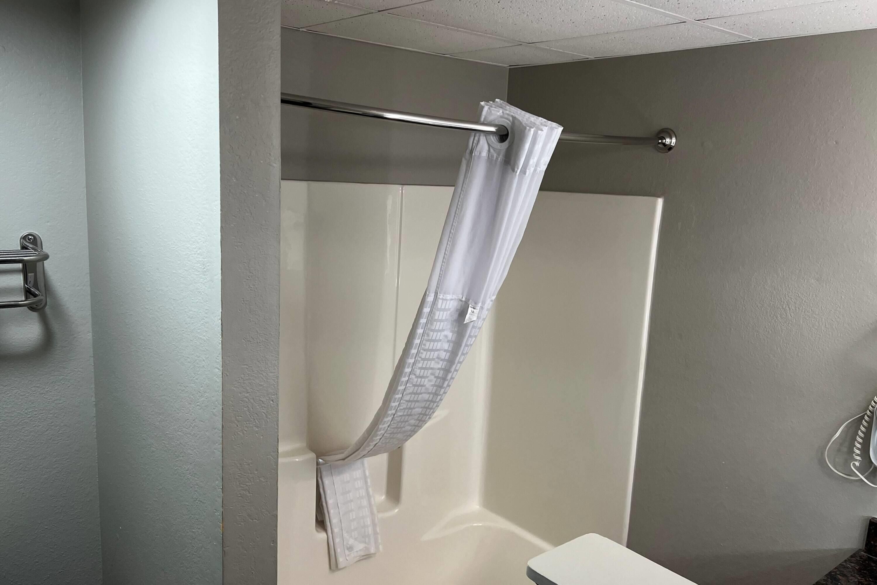 A shower with a white curtain, a metal towel rack, and a white sink.
