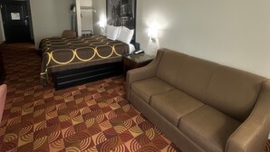 Une chambre d’hôtel avec une moquette à motifs, un lit avec une tête de lit, un canapé marron, une table de chevet et un tableau encadré au mur.
