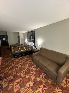 Ein Hotelzimmer mit einem gemusterten Teppich, einem Bett mit Kopfteil, einem braunen Sofa, einem Nachttisch und einem gerahmten Bild an der Wand.