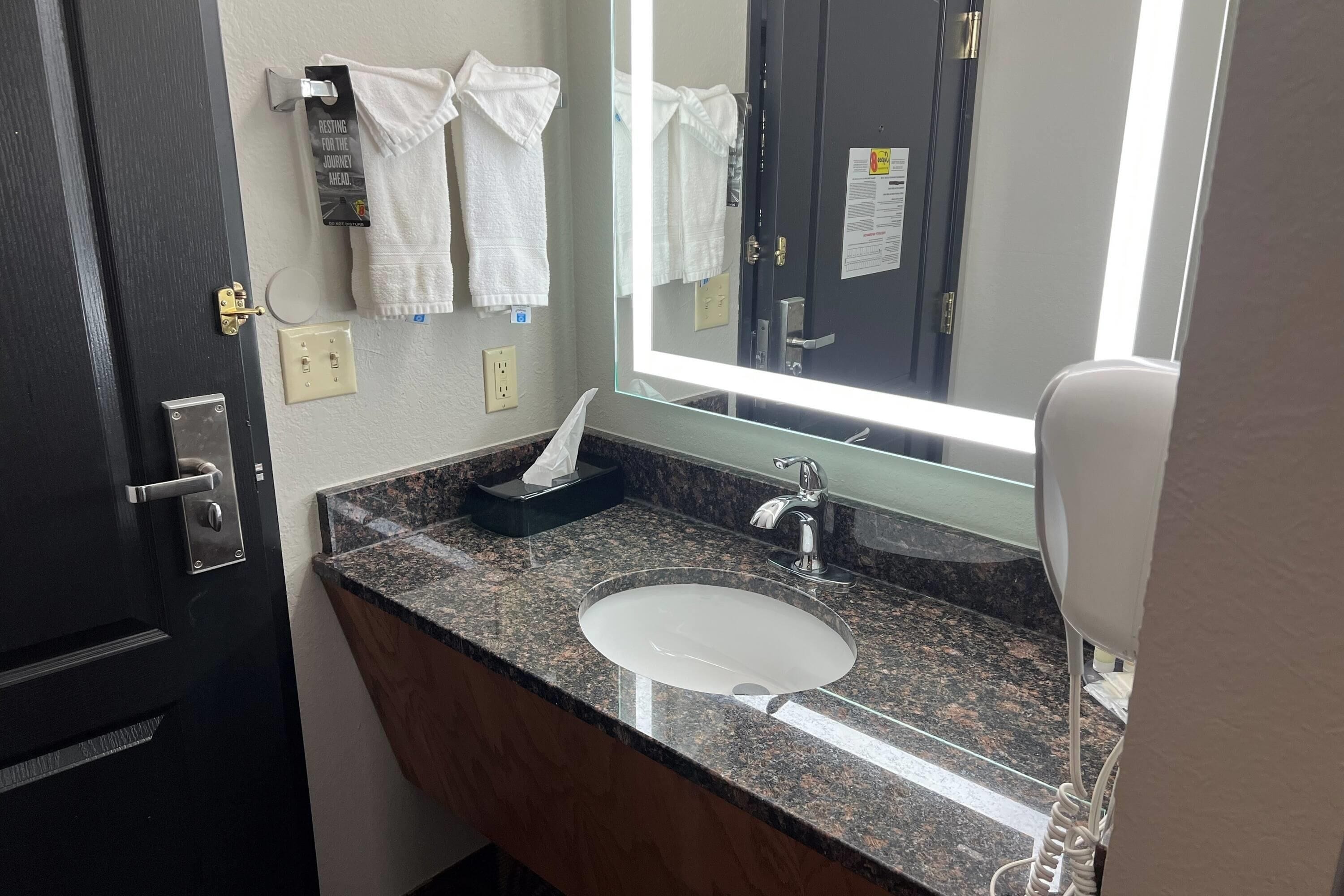 A bathroom with a sink, mirror, towel rack, and a towel dispenser.
