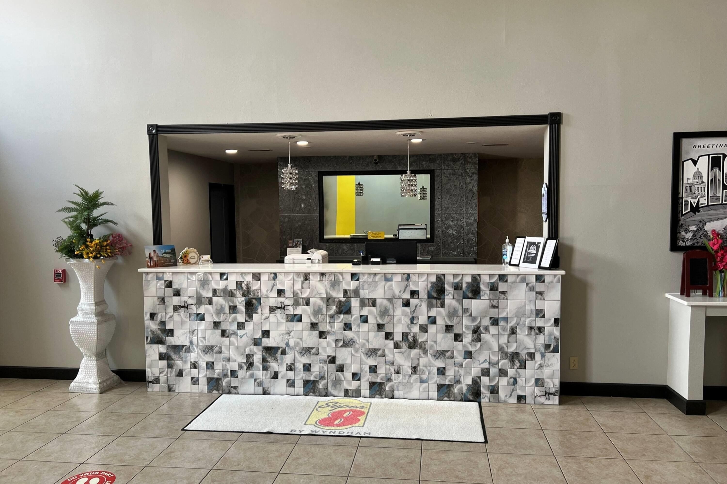 Un comptoir d’accueil orné de motifs géométriques en carreaux, un miroir au-dessus et un détecteur d’incendie sur le mur.