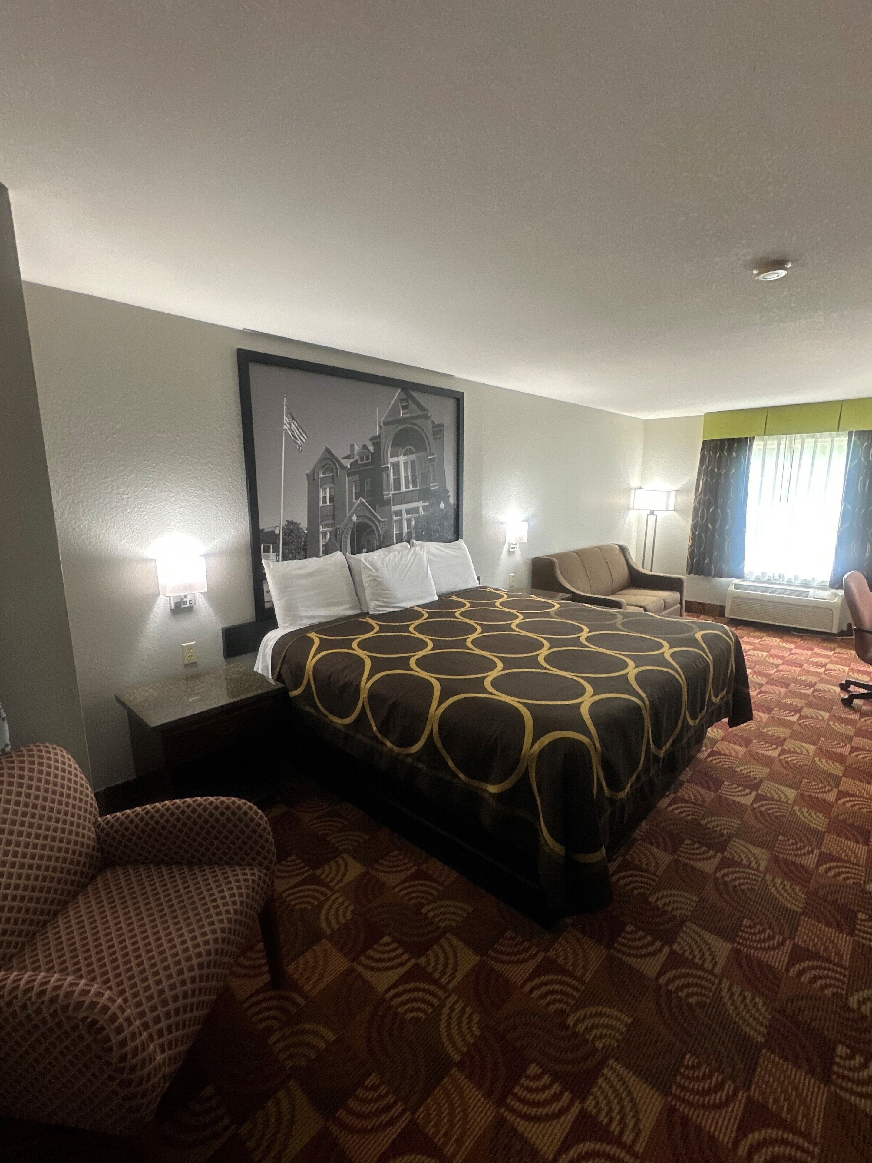 Een hotelkamer met een groot bed, een bureau, een stoel en een schilderij aan de muur.