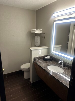 A bathroom with a toilet, sink, and mirror. There is a towel rack with folded towels and a sign that says "Laundry Bag." - Super 8 by Wyndham Lake of the Ozarks (Eldon)
