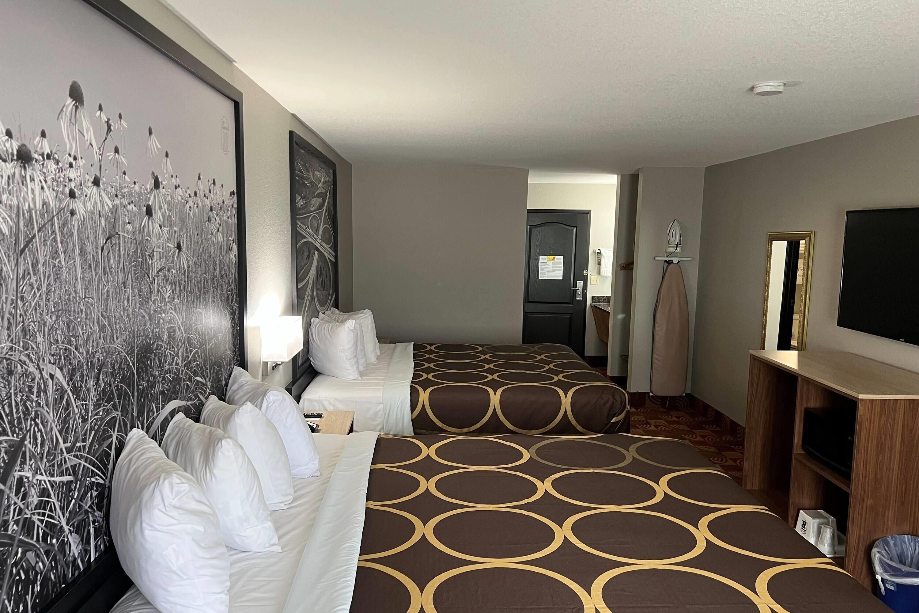 A hotel room with a large bed, a TV, a desk, and a painting on the wall.