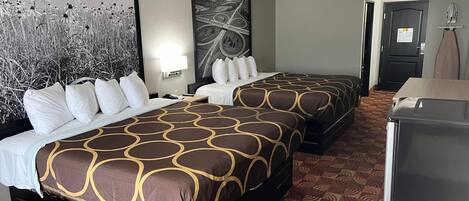 A hotel room with two beds, a large painting on the wall, a desk with a lamp, and a refrigerator.