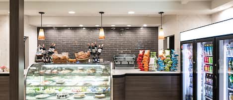 Un área moderna de comidas con mostrador de delicatessen, vitrinas refrigeradas y lámparas colgantes.