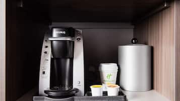 Keurig-kahvinkeitin, jossa on kahvikapseli, kaksi kertakäyttöistä kuppia ja suuri säiliö, todennäköisesti kahvinporoja varten, keittiön kaapissa.