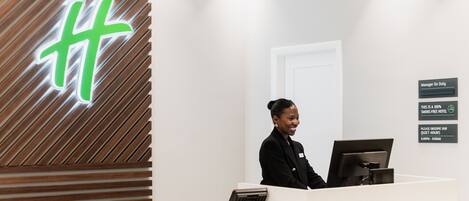 A hotel reception desk with a modern design, a digital sign displaying a logo, and a sign indicating quiet hours.