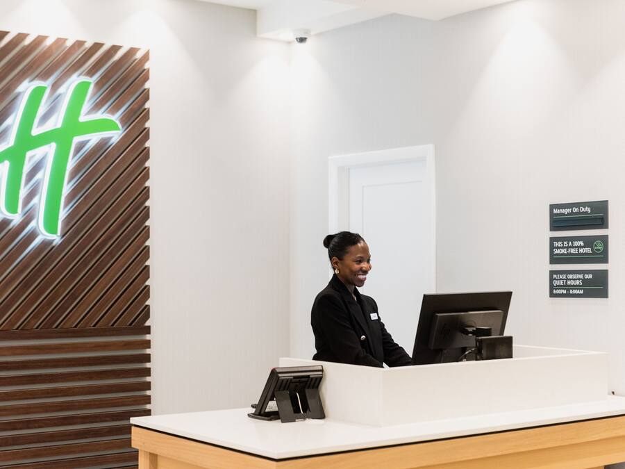Un mostrador de recepción de hotel con diseño moderno, un letrero digital que muestra un logotipo y un aviso sobre las horas de silencio.