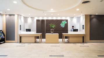 A reception area with two reception desks, a potted plant, and a wall with a geometric pattern and a neon sign.