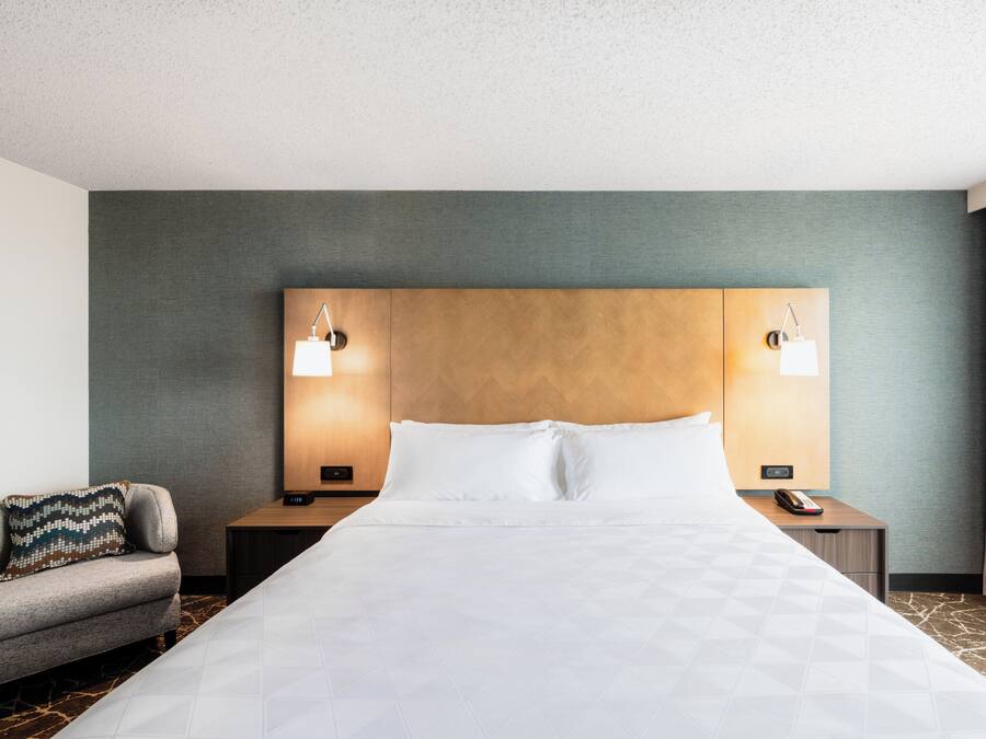 A hotel room with a large bed, two bedside tables with lamps, a sofa, and a view of the outdoors.