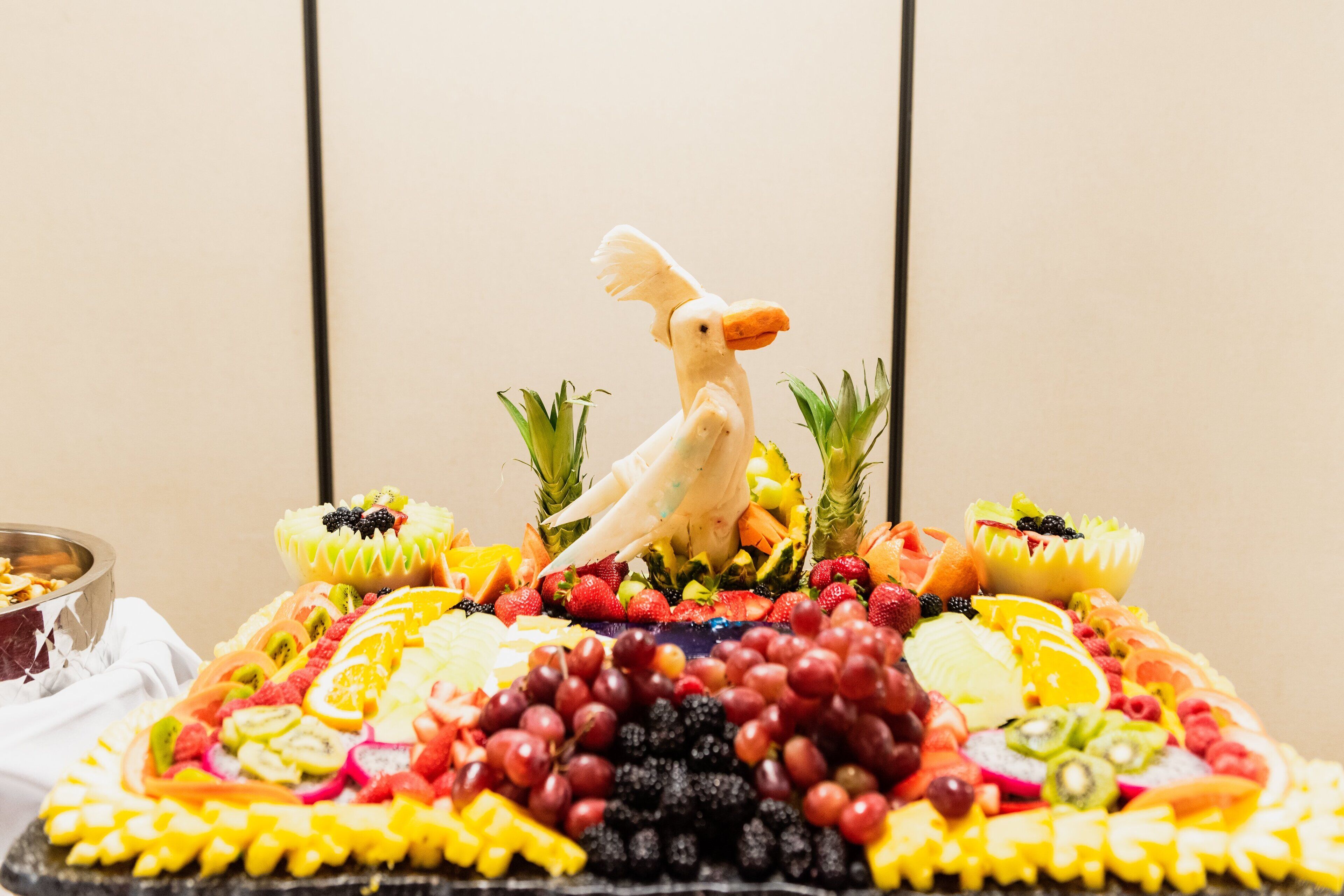 A fruit platter with a bird decoration, surrounded by tropical fruits and berries.