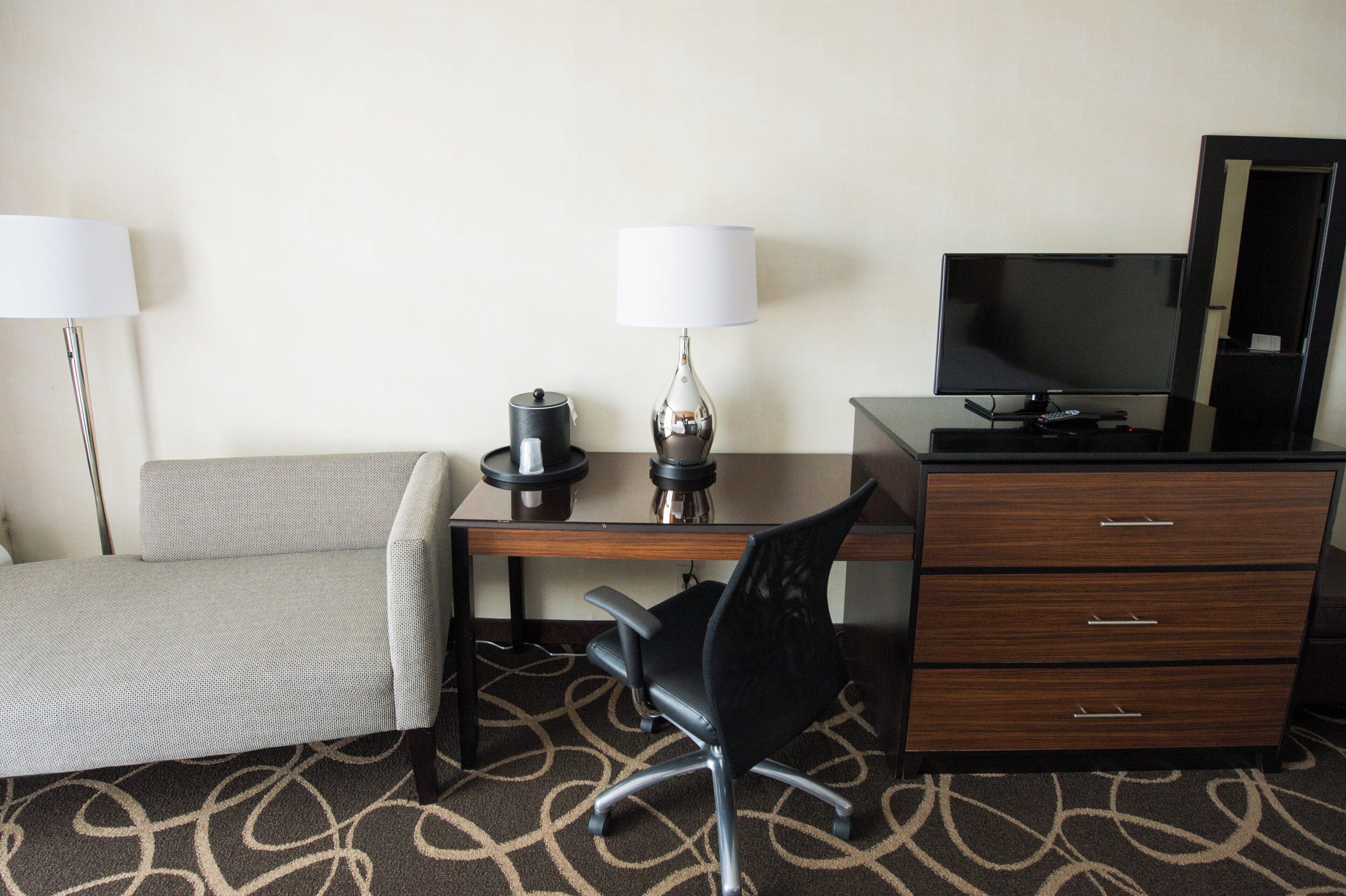 Une chambre d’hôtel comprenant un lit, un bureau avec une lampe, une chaise, une télévision et une commode.