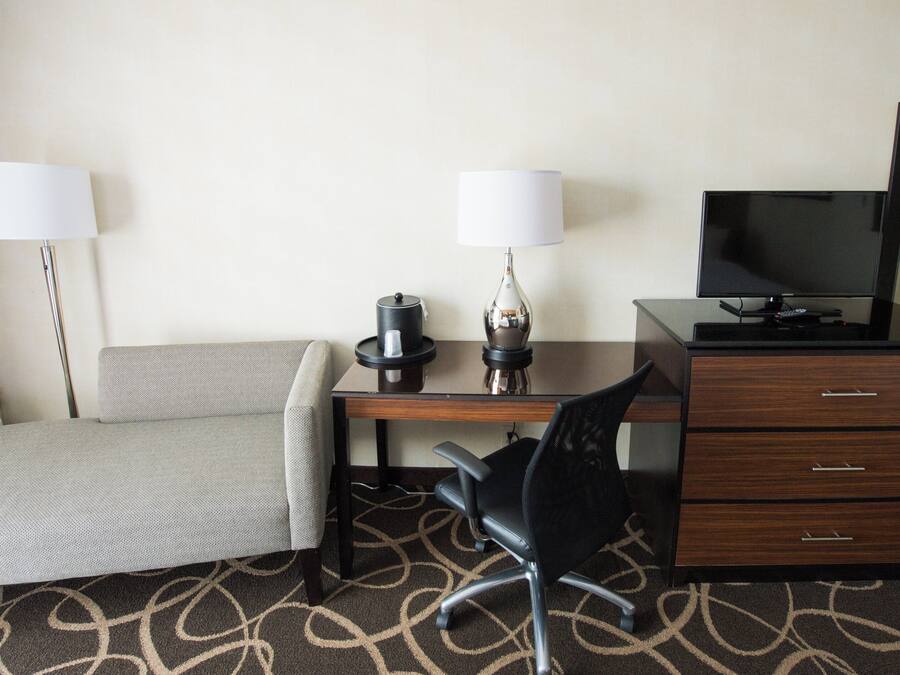 A hotel room with a bed, a desk with a lamp, a chair, a television, and a dresser.