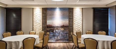 A conference room with a round table, beige chairs, and a large abstract painting on the wall.