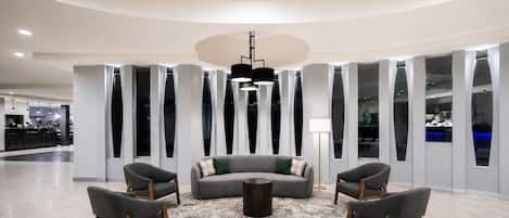 A modern lobby with a round coffee table, grey sofas, and wooden chairs.