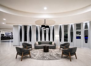 A modern lobby with a round coffee table, grey sofas, and wooden chairs. - Holiday Inn Newark International Airport by IHG (Newark)