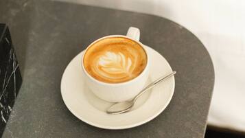 Uma chávena de café com arte de latte sobre um pires branco, colocada sobre uma mesa de mármore escuro.