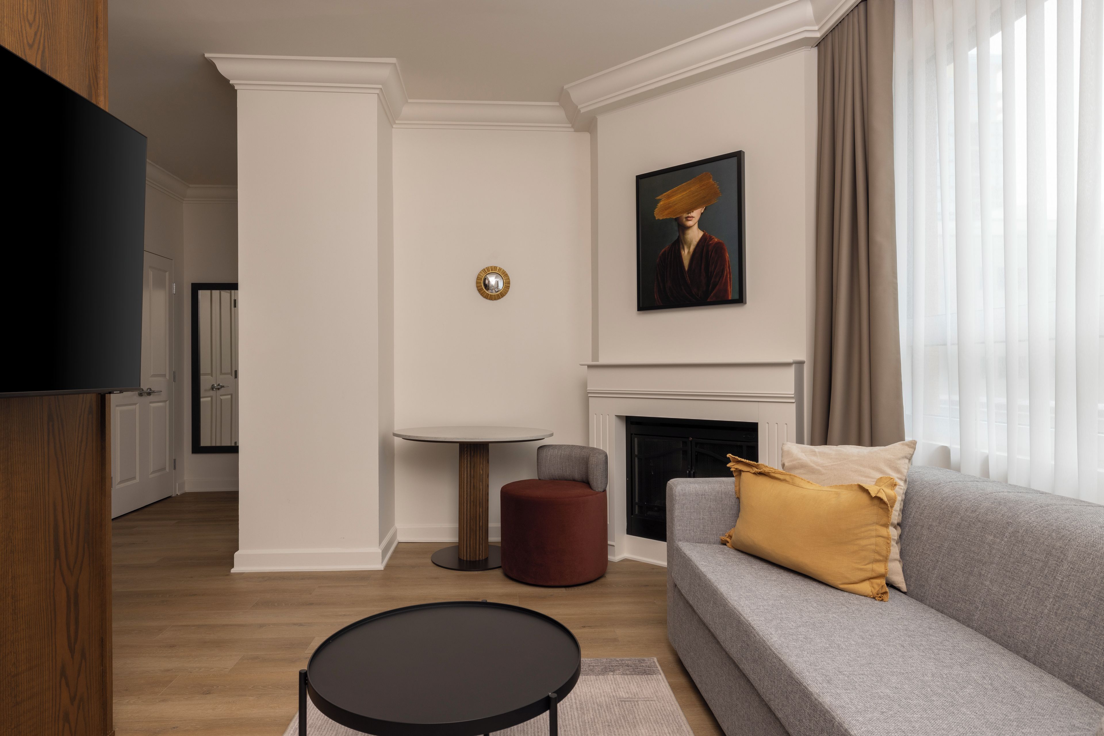 Un salon moderne avec un canapé gris, une table basse ronde, une cheminée et un tableau accroché au mur.