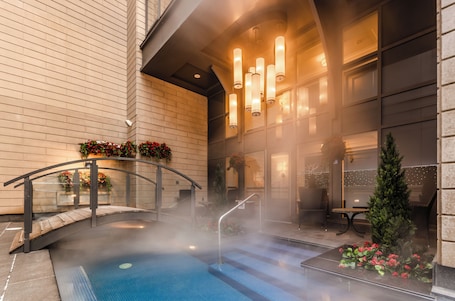 A heated outdoor pool area with a glass balustrade, a small bridge, and a Christmas tree.. Metcalfe Hotel Montréal by Gray Collection