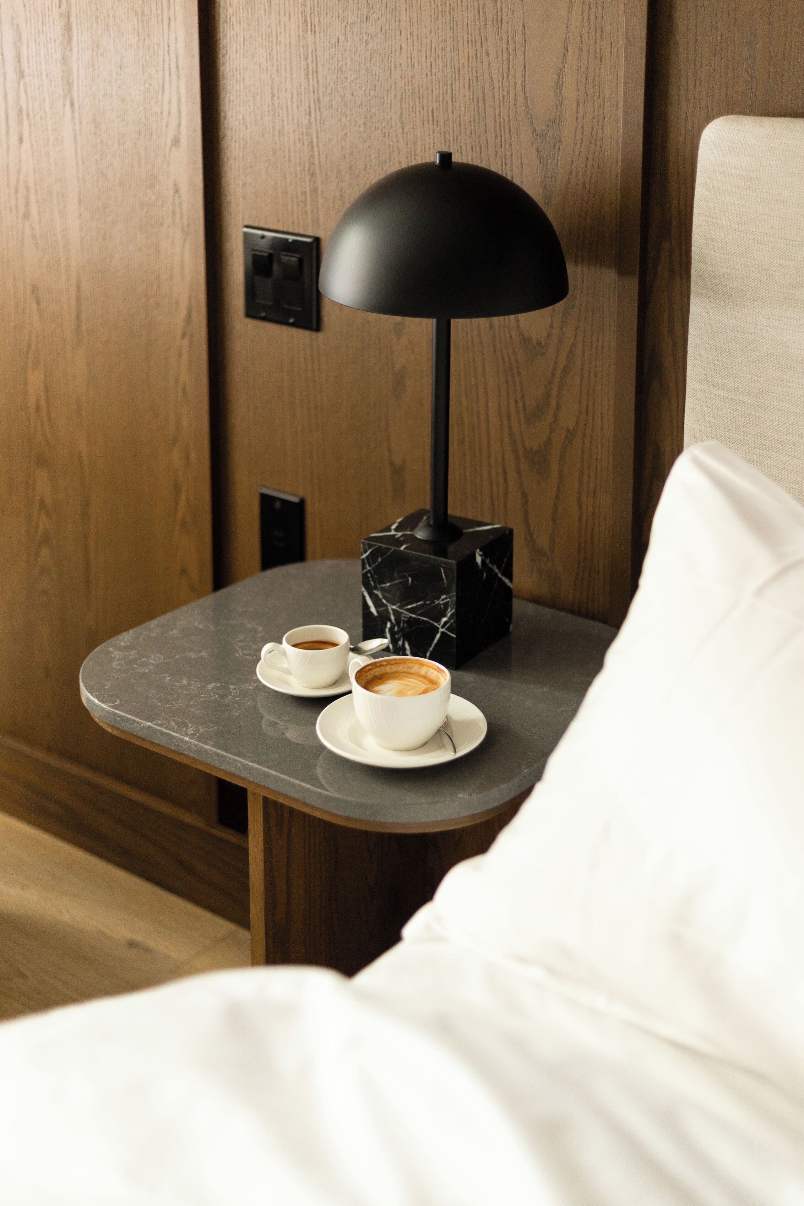 A small table with two cups of coffee, a black lamp, and a marble box.