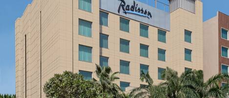 Un hôtel Radisson au design moderne, doté d’une enseigne bien visible, de plusieurs étages et d’un espace d’entrée aménagé avec des palmiers et des arbustes.