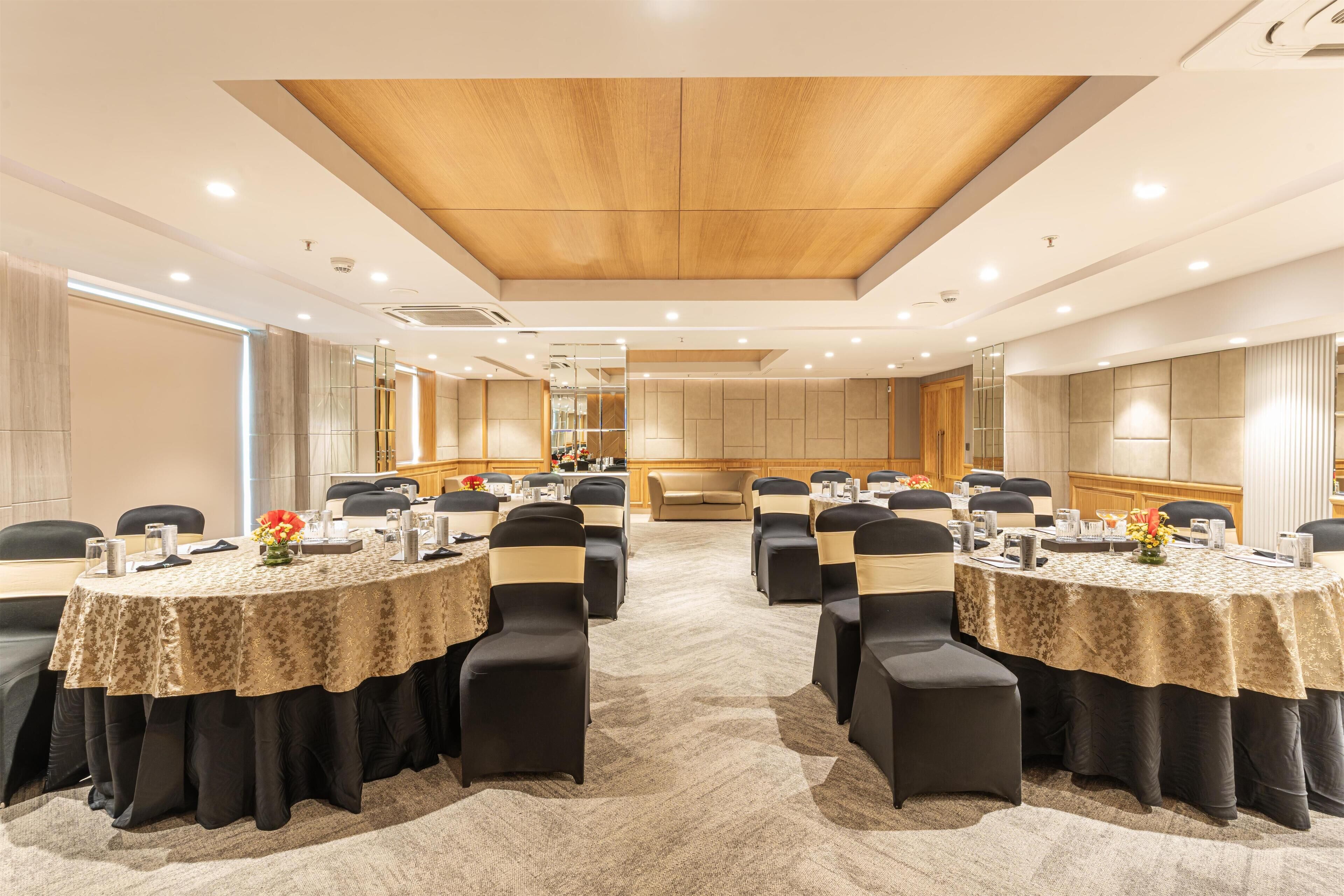 A conference room with round tables, black chairs, and beige tablecloths.