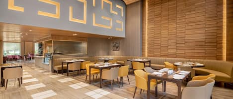 Een modern restaurant met een geometrisch wandontwerp, houten lambrisering en een mix aan zitplaatsen, waaronder tafels en hoekbanken.