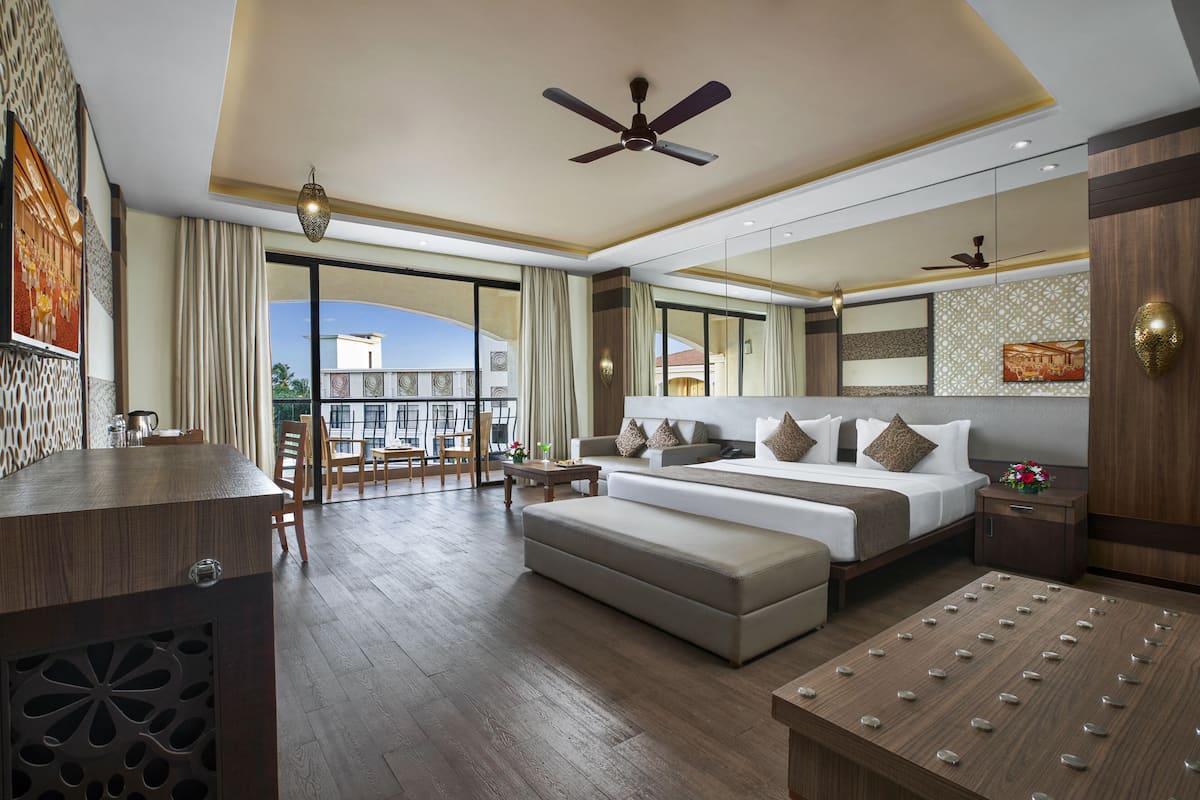 A spacious hotel room with a large bed, a sofa, a dining table, and a balcony with a view.