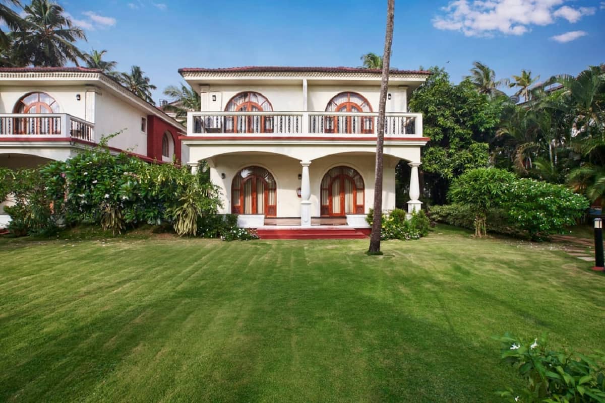 A two-story house with a balcony, surrounded by lush greenery and a well-maintained lawn.