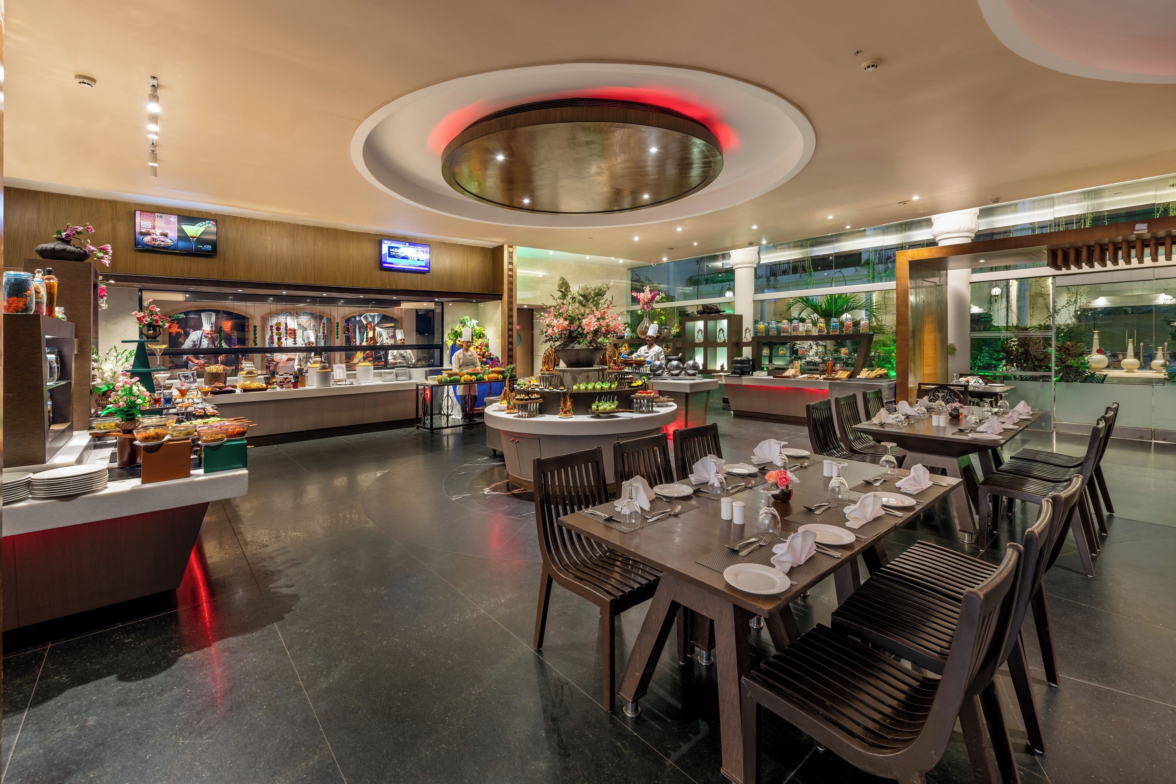 A modern restaurant with a central island, multiple dining tables, and a variety of food displays.