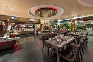 A modern restaurant with a central island, multiple dining tables, and a variety of food displays.