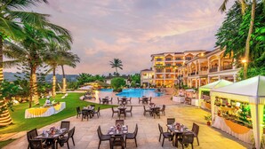 An outdoor dining area with tables and chairs, a pool, and a building with balconies.