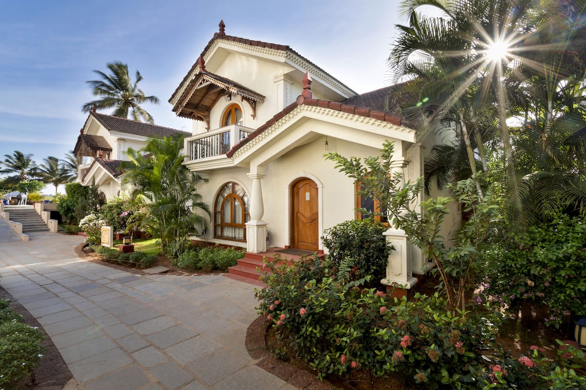 A two-story house with a balcony, surrounded by lush greenery and palm trees.