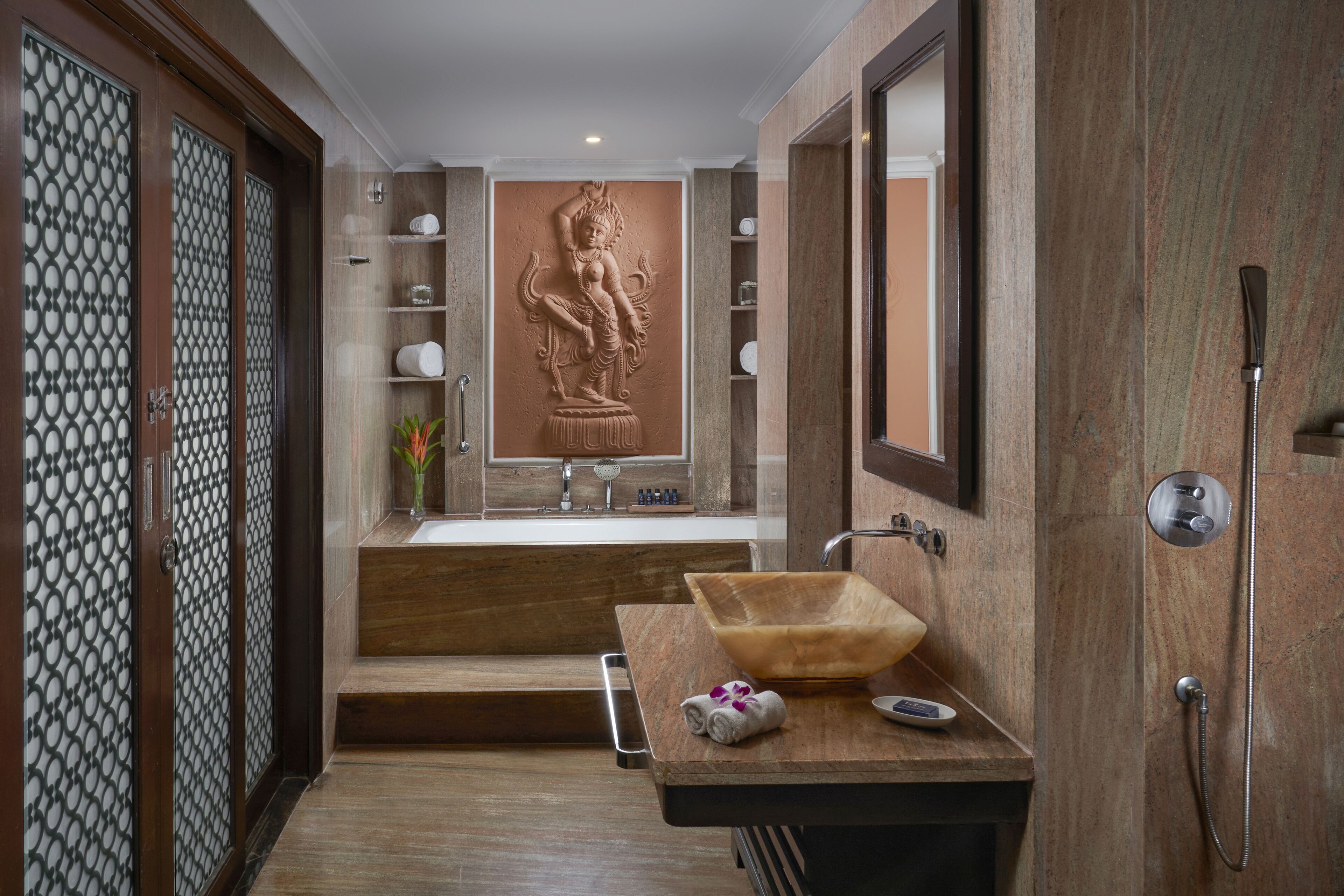 Un baño moderno con tocador de madera, un espejo grande y una escultura decorativa en la pared.