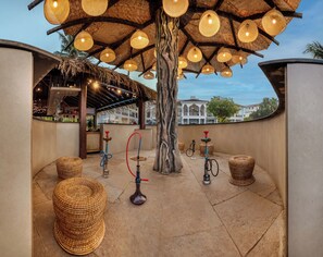 An outdoor seating area with woven furniture, hanging lights, and hookahs.